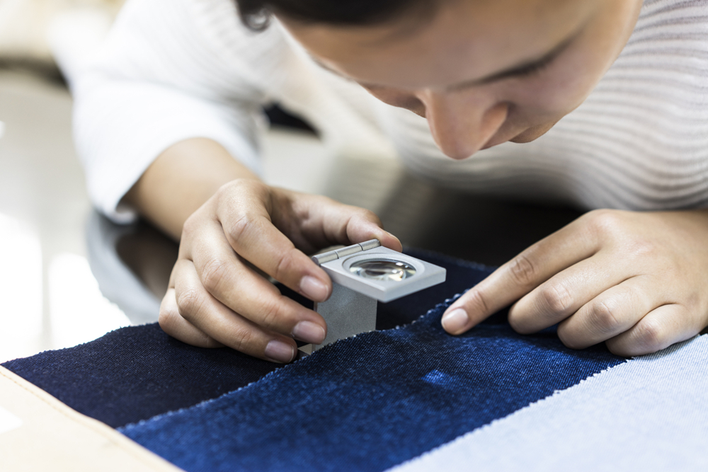 Young woman examining fabric quality with magnifier