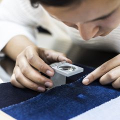 Young woman examining fabric quality with magnifier
